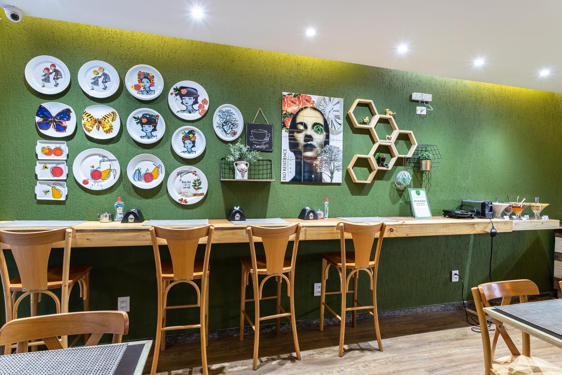 A restaurant with a green wall, wooden chairs, and a variety of colorful plates displayed on the wall.