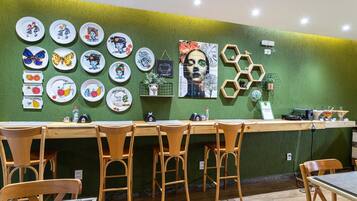A restaurant with a green wall, wooden chairs, and a variety of colorful plates displayed on the wall.