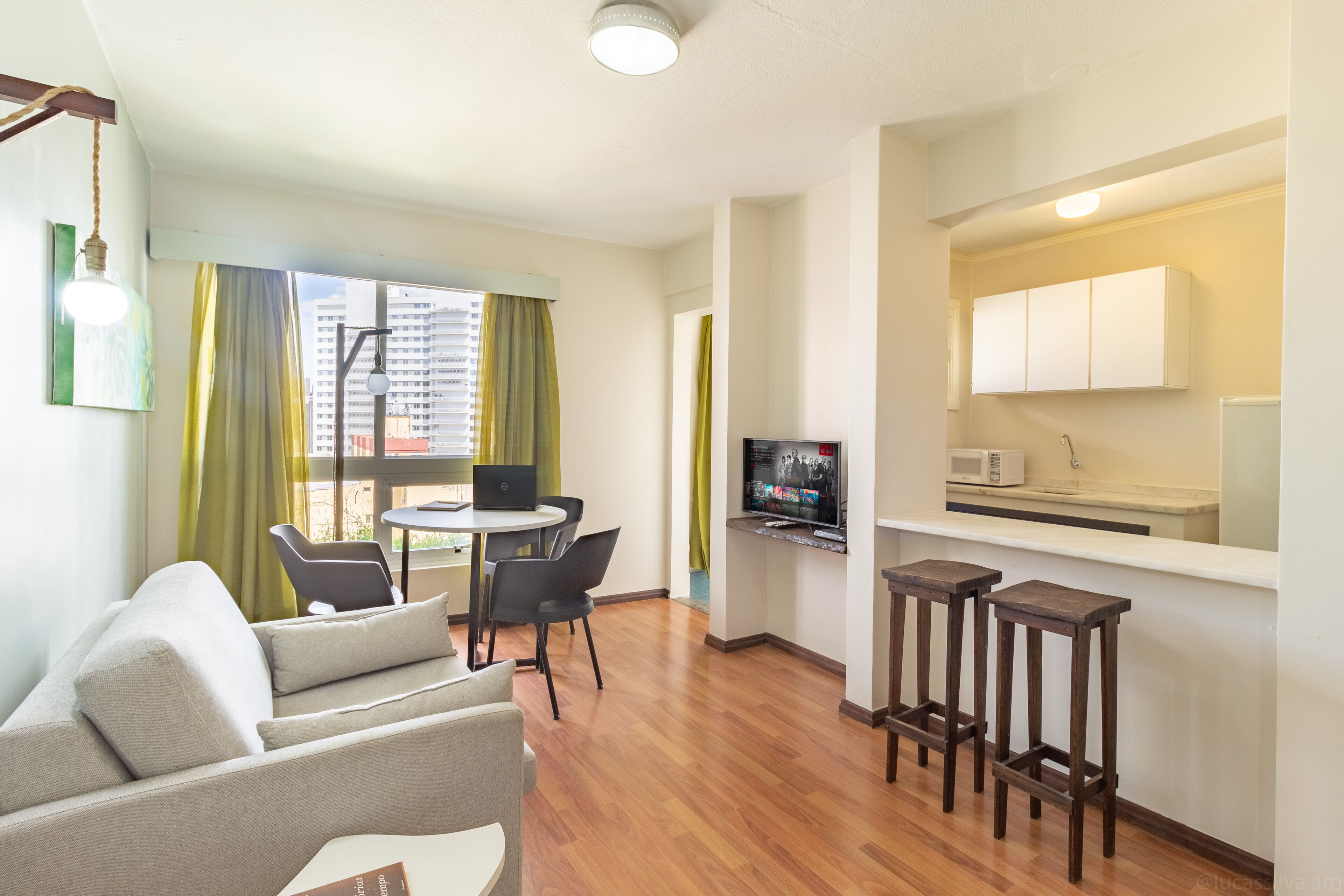 Een modern appartement met woonkamer, eetgedeelte en kitchenette. Het heeft een bank, eettafel, stoelen, een televisie en een klein barretje.