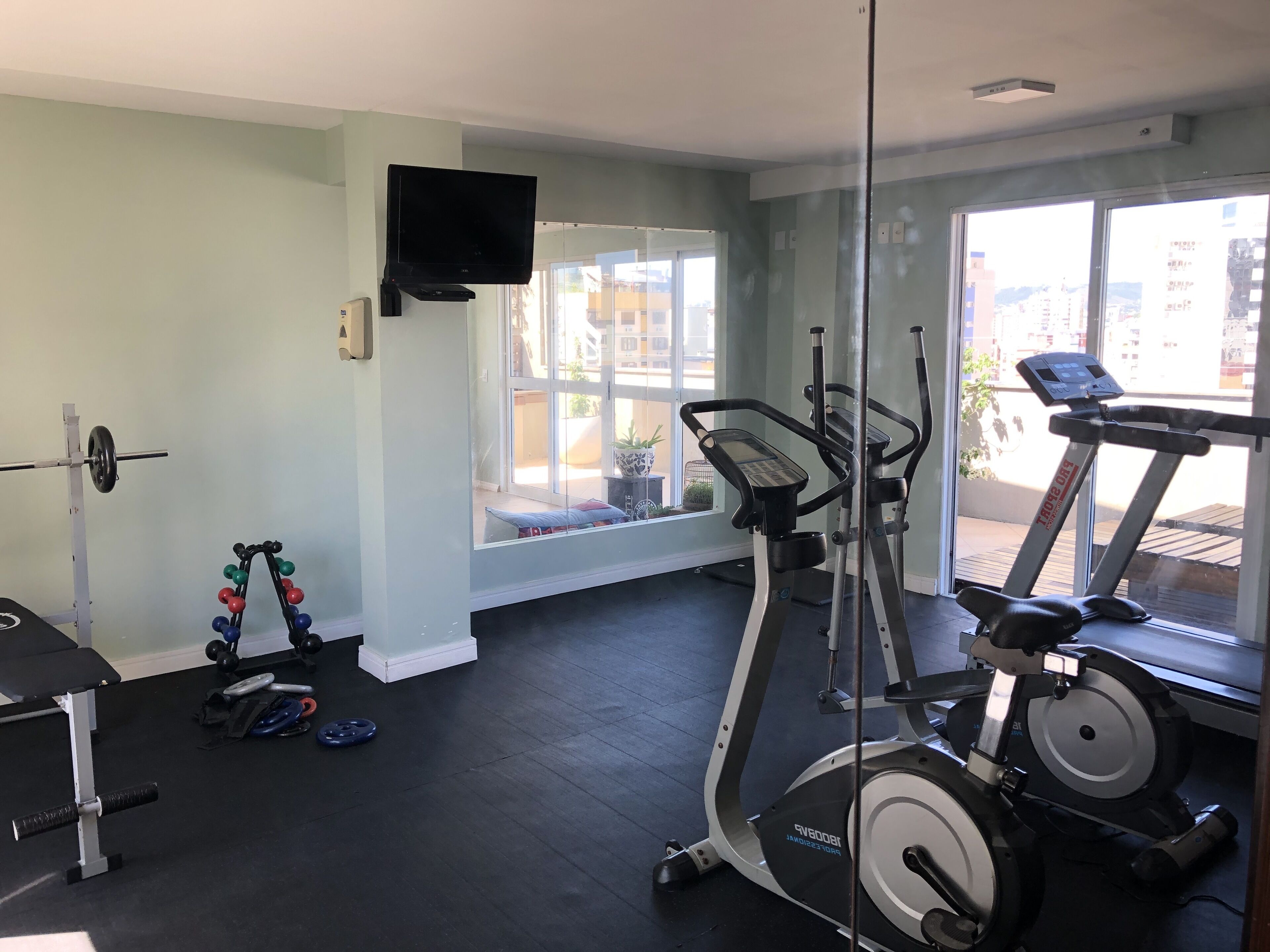 Een sportschool met trainingsapparatuur, een loopband en een televisie aan de muur.