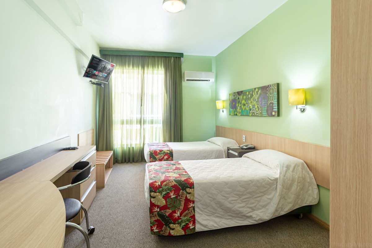 Habitación de hotel con dos camas, un escritorio, una silla, un televisor y una ventana con cortinas.