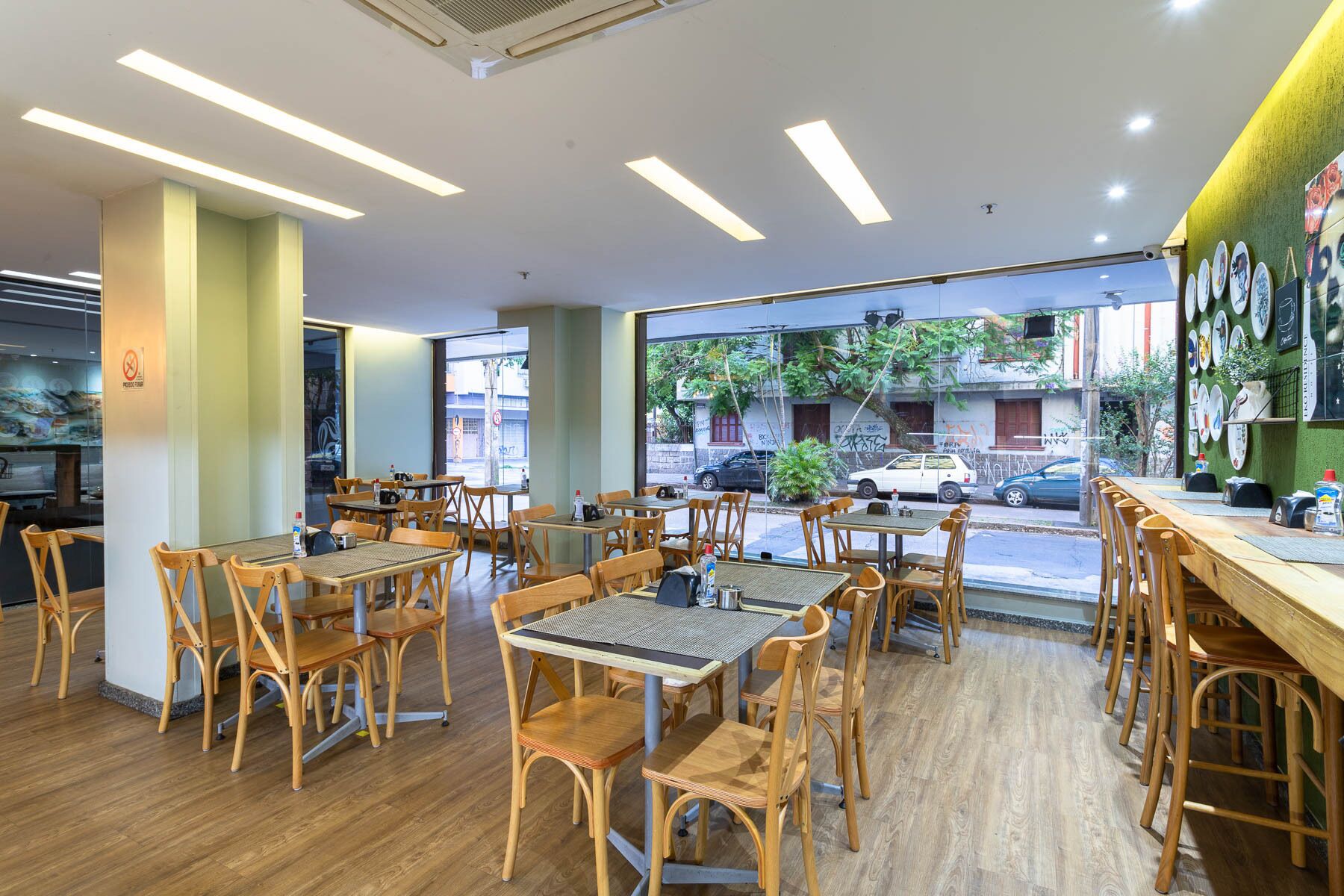 Un restaurante con mesas y sillas de madera, amplios ventanales y vistas a la calle.