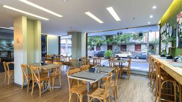 Un restaurante con mesas y sillas de madera, amplios ventanales y vistas a la calle.