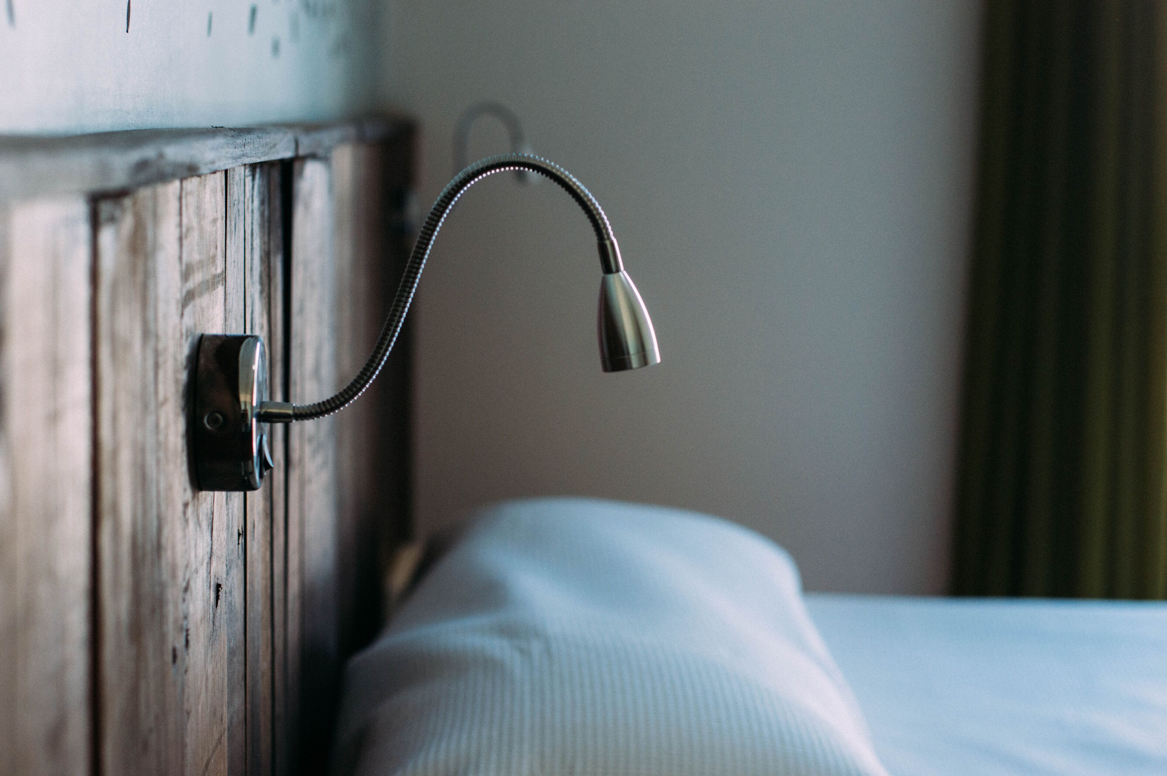 A bed with a wooden headboard and a metal lamp attached to it.