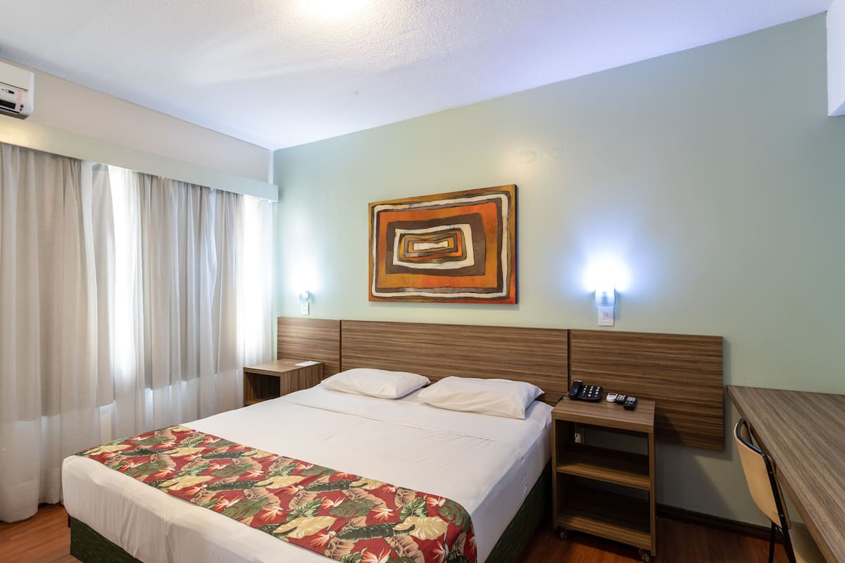 Una habitación de hotel con cama, mesita de noche, escritorio y una obra de arte colgada en la pared.