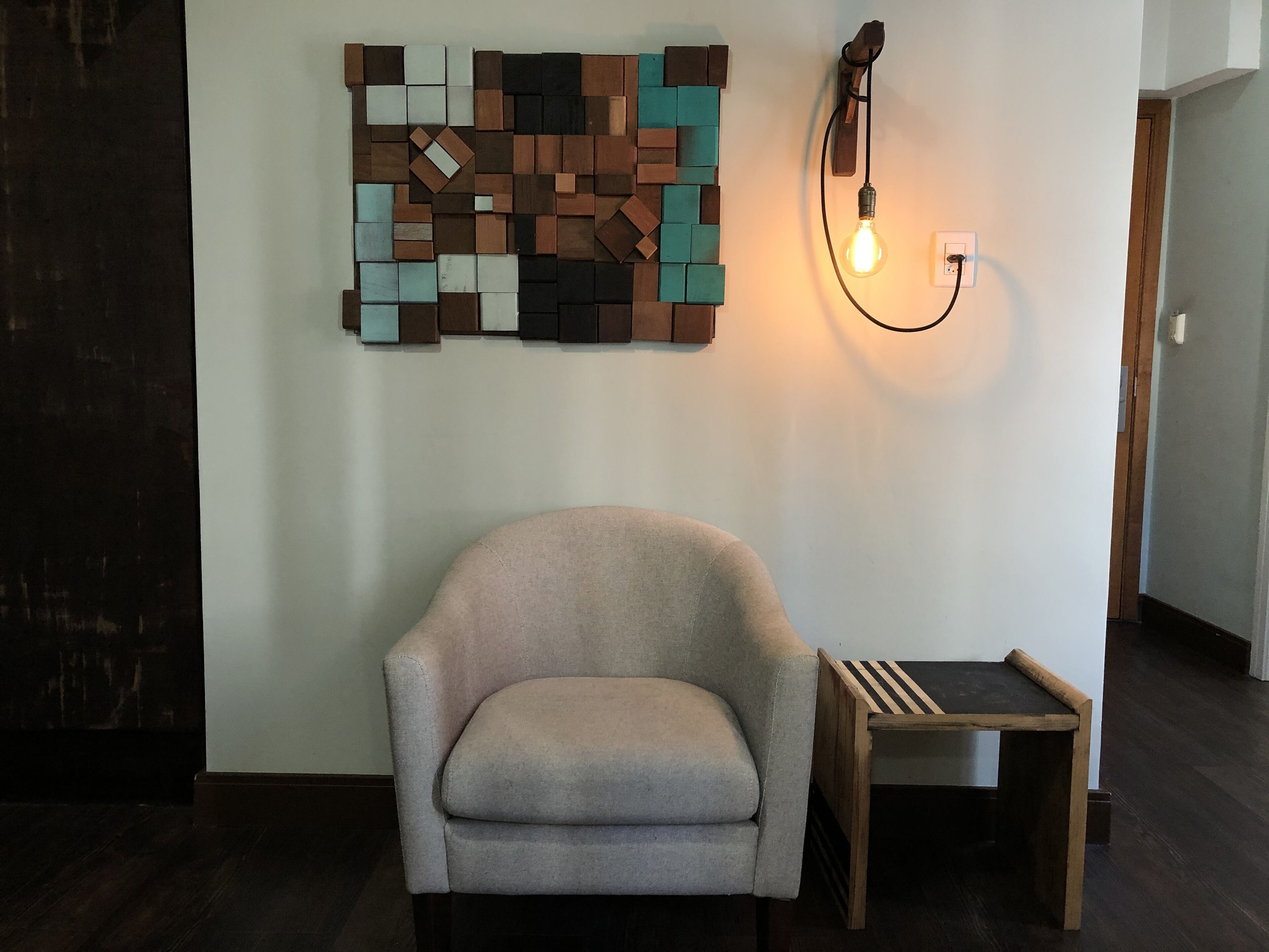 A room with a light-colored armchair, a small wooden side table, and a wall-mounted light fixture.