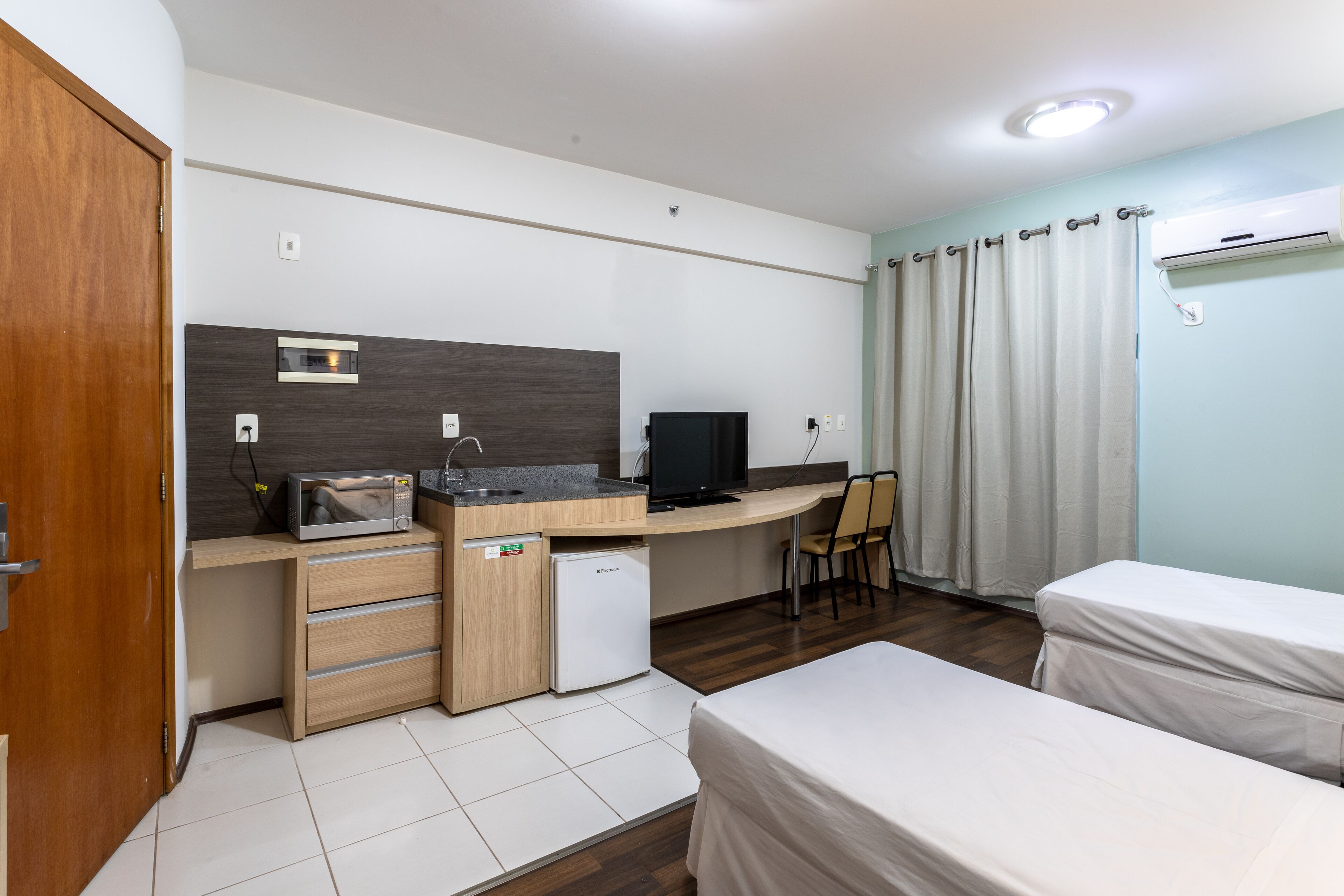 Una habitación de hotel compacta con kitchenette, cama, escritorio y televisor.