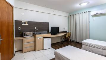 Una habitación de hotel compacta con kitchenette, cama, escritorio y televisor.