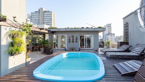 Un área de piscina al aire libre con terraza de madera, sillas de descanso y plantas en macetas.