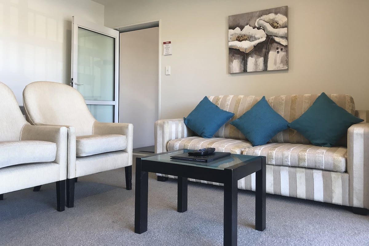 Een woonkamer met een gestreept bankstel, twee fauteuils, een glazen salontafel en een schilderij aan de muur.