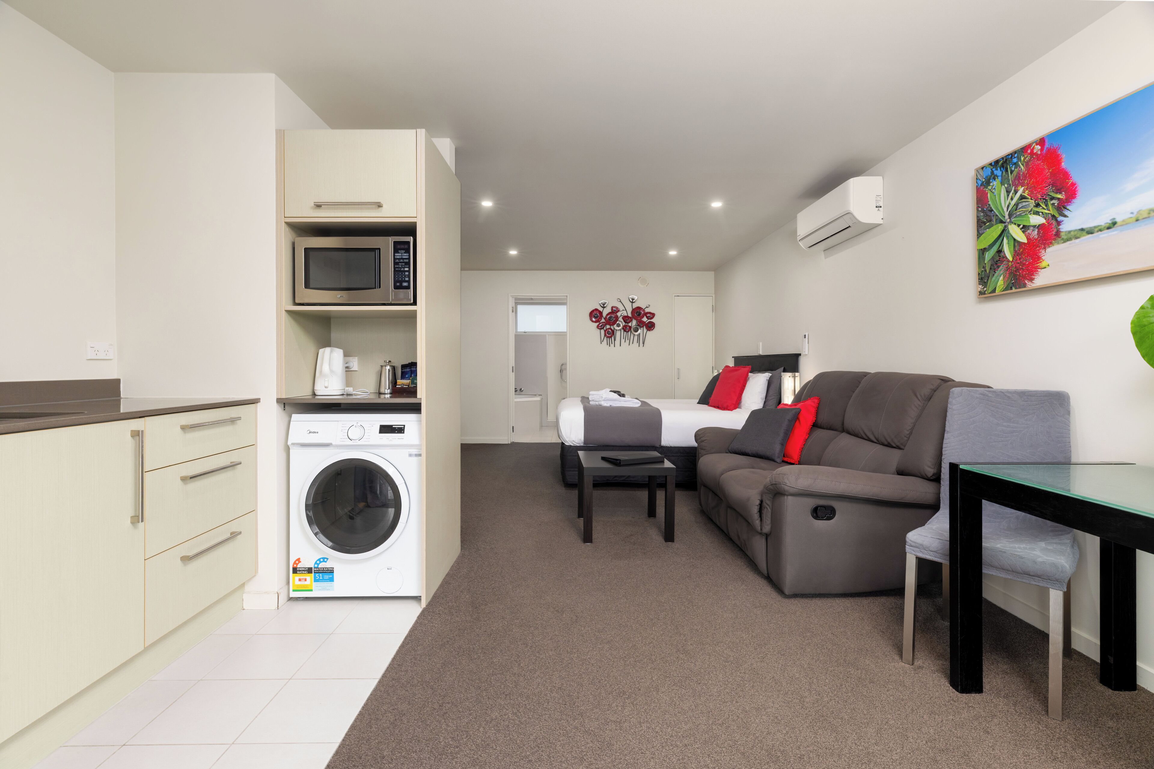 A compact living space with a kitchenette, a washing machine, a sofa, a dining table, and a bed.