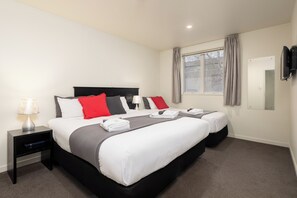 Quarto de hotel com uma cama grande, mesa de cabeceira com luminária, janela com cortinas e televisão de tela plana fixada na parede.