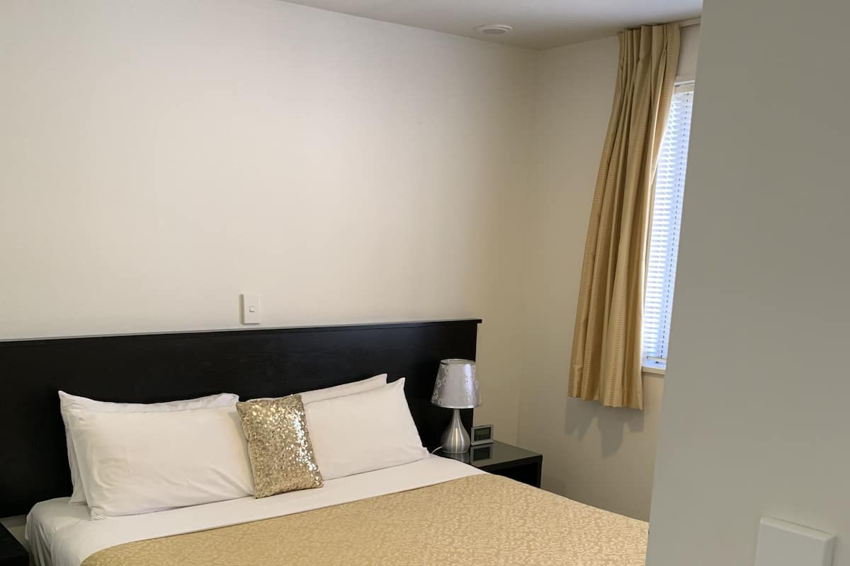 Een net opgemaakt bed met een bedspreide met een patroon, een zwart hoofdeinde en een bedlamp.