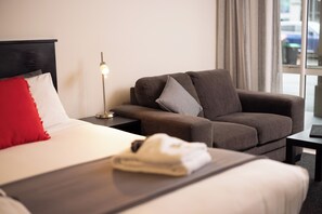 Een hotelkamer met een bed, een slaapbank, een nachtkastje met een lamp en een raam met gordijnen.