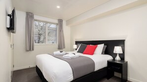 A modern hotel room with a large bed, a bedside table with a lamp, and a window with curtains. - Salerno Motel Apartments (Christchurch)