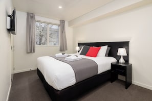 Une chambre d’hôtel moderne avec un grand lit, une table de chevet avec une lampe et une fenêtre avec des rideaux.