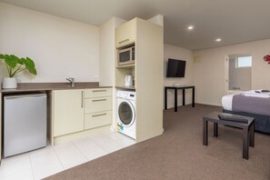 Une chambre d’hôtel compacte équipée d’une kitchenette, d’un lave-linge, d’un lit et d’un téléviseur.