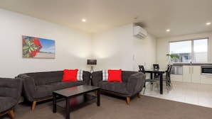 A modern living room with a sectional sofa, a coffee table, and a dining area with a table and chairs. - Salerno Motel Apartments (Christchurch)