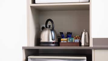 Uma bancada com micro-ondas, chaleira e cafeteira em uma prateleira, e uma pequena geladeira abaixo.