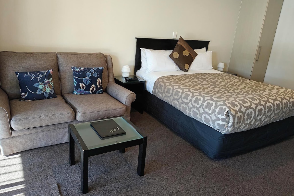 Een hotelkamer met een bank, een bed, een nachtkastje en een klein tafeltje.