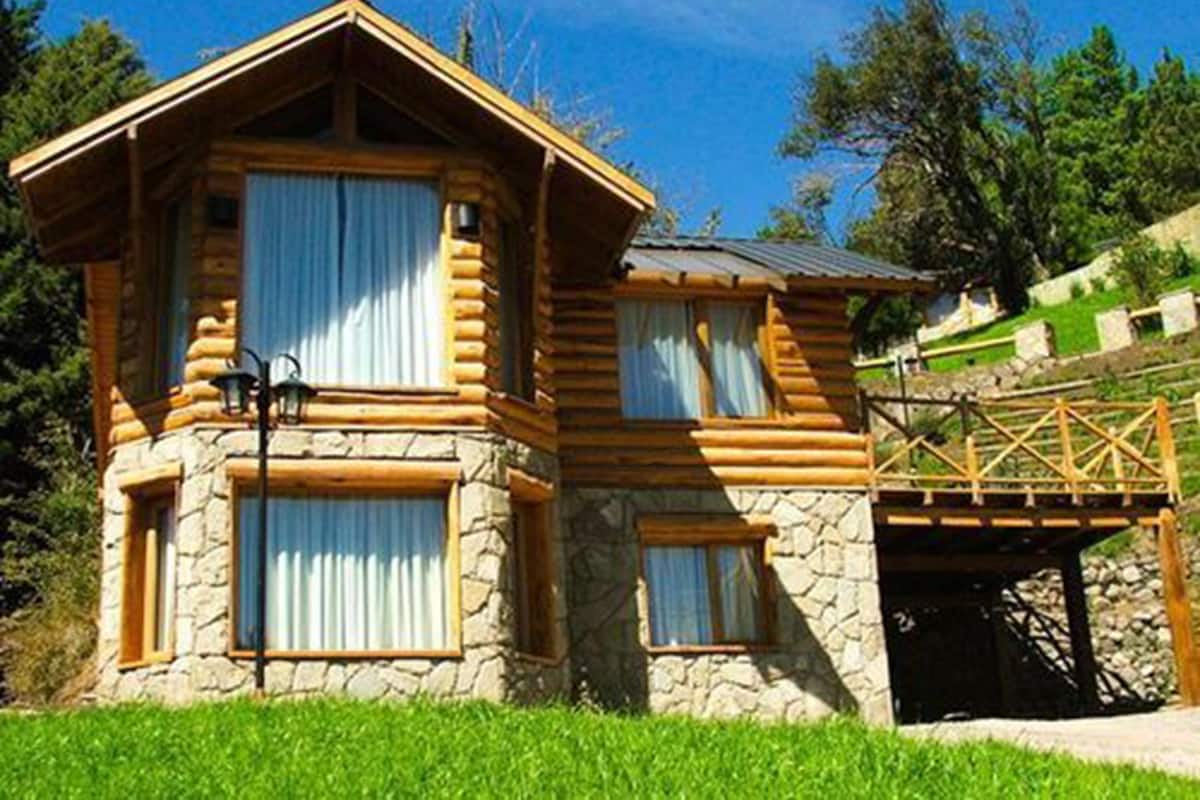 A log cabin with stone walls, large windows with curtains, and a wooden deck.