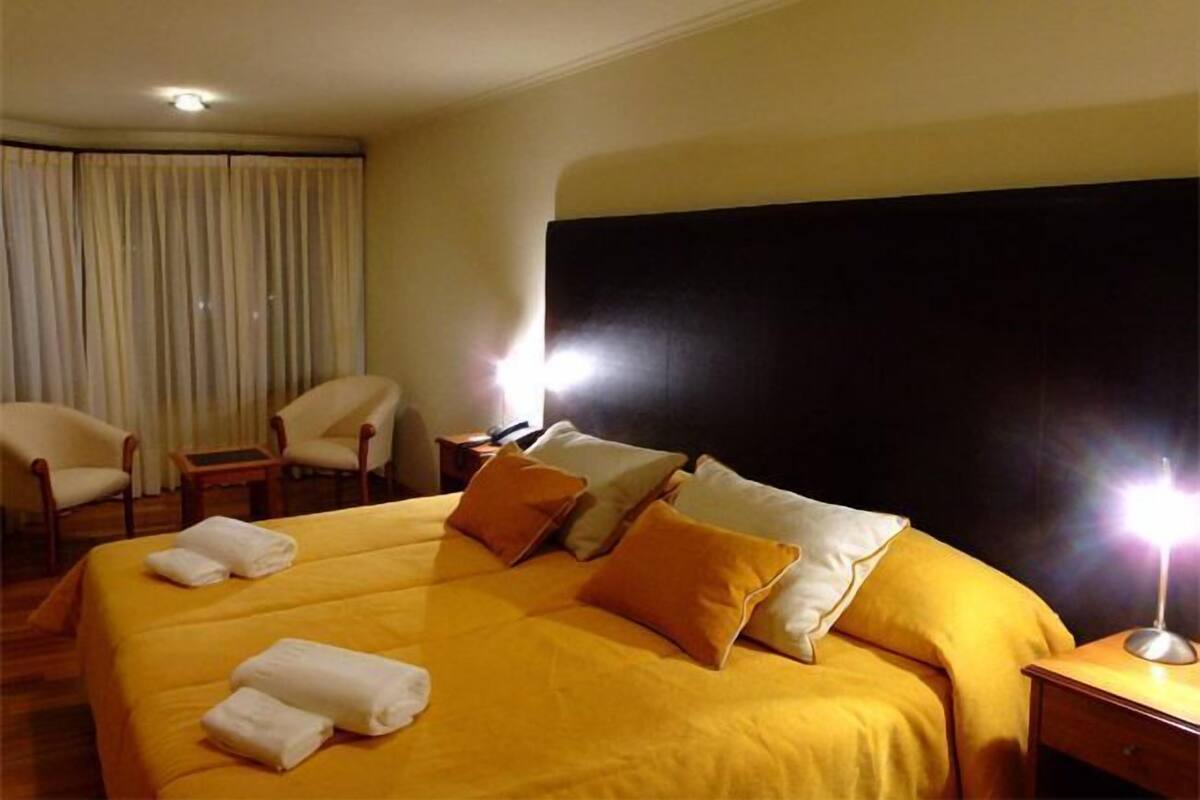 A hotel room with a large bed, two chairs, a nightstand, and a lamp.
