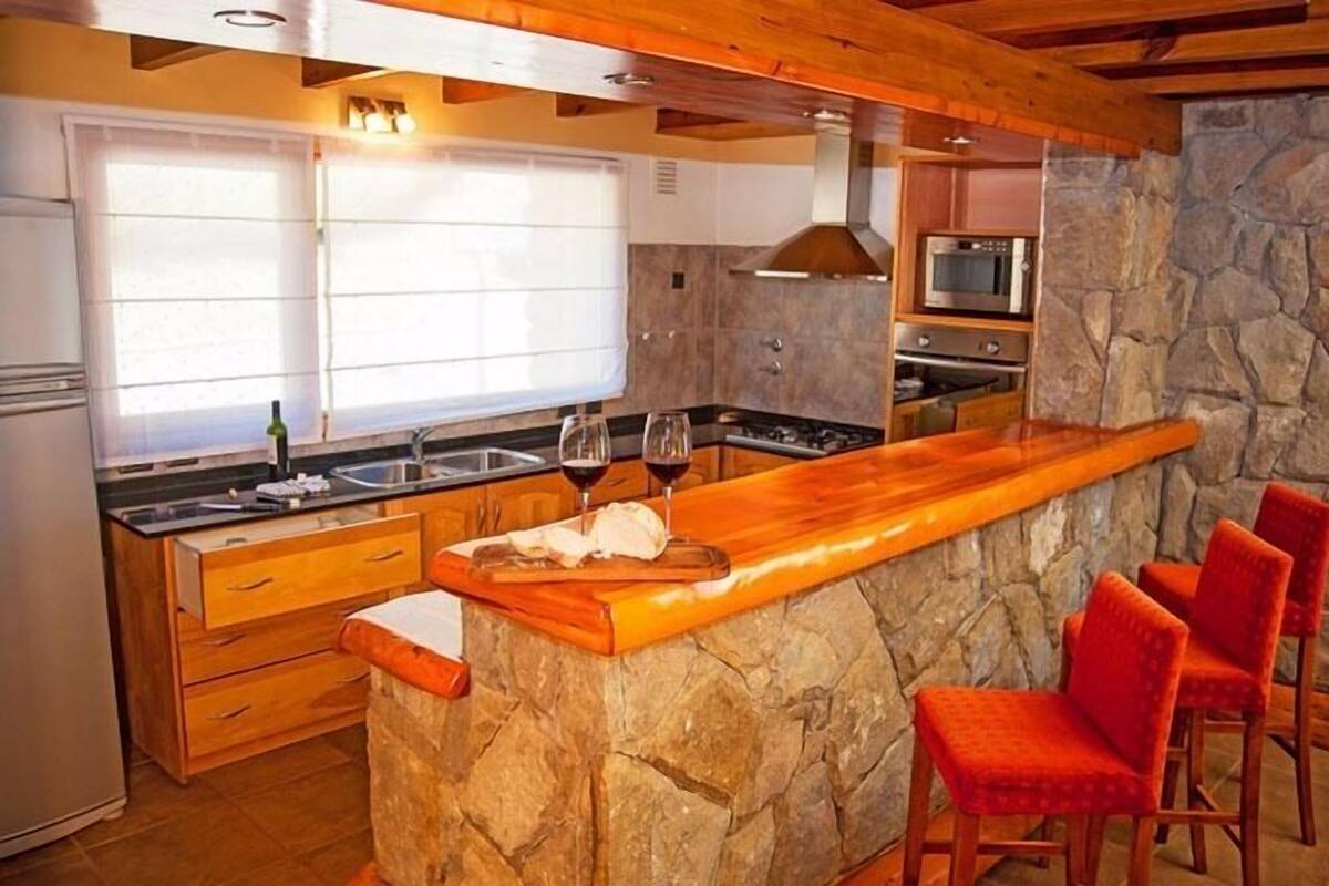 A kitchen with a stone island, wooden bar, and red chairs.