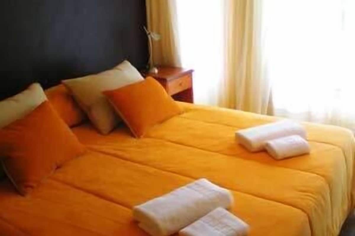 A hotel room with a large bed, two pillows, a nightstand, and a window with curtains.