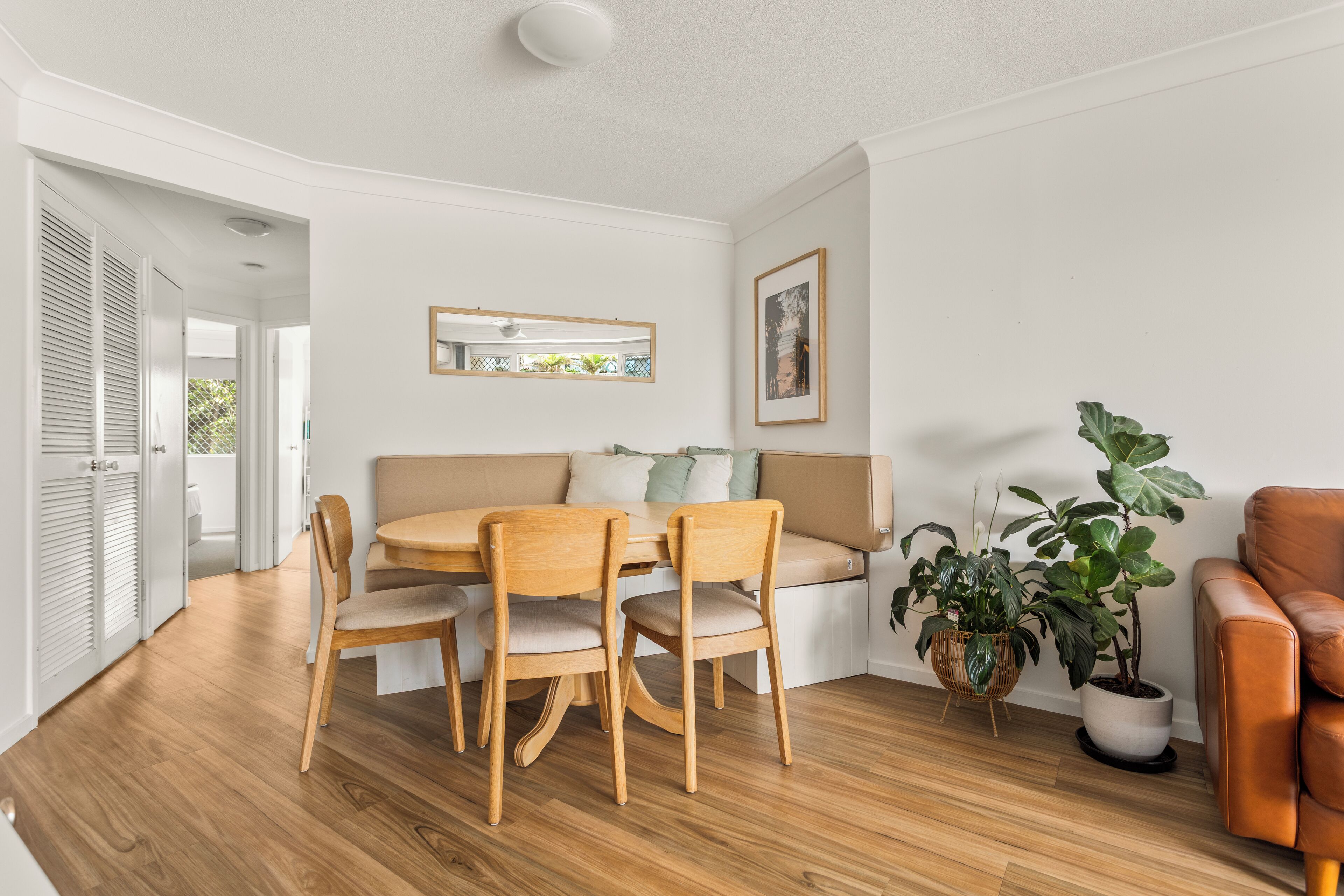 A modern living room with a wooden dining table and chairs, a sofa, a brown leather armchair, and a potted plant.