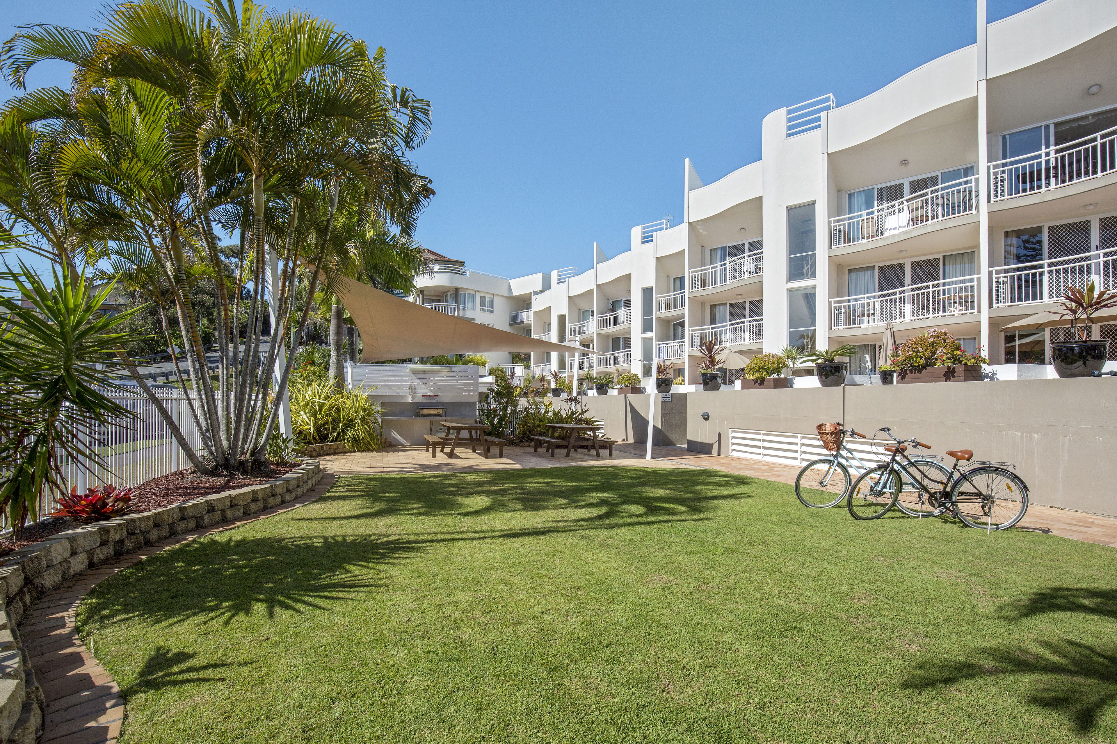 A hotel with multiple balconies, a grassy courtyard, and bicycles parked outside.