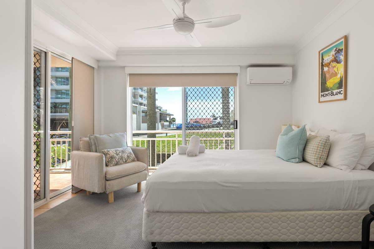Een hotelkamer met een bed, een stoel, een balkon met uitzicht en een plafondventilator.