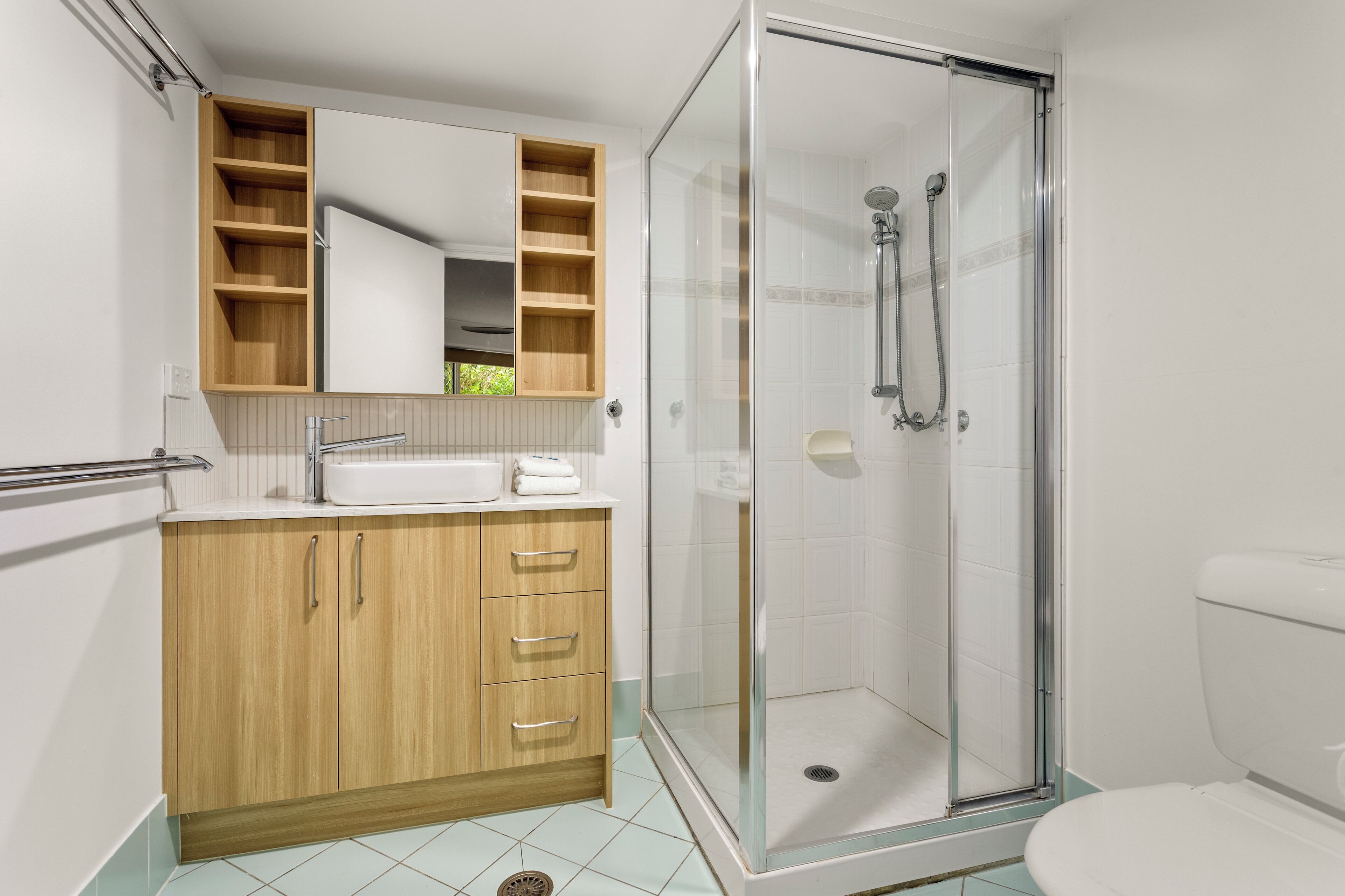 Une salle de bain moderne avec une douche à parois de verre, un meuble-lavabo en bois avec un miroir et des toilettes blanches.