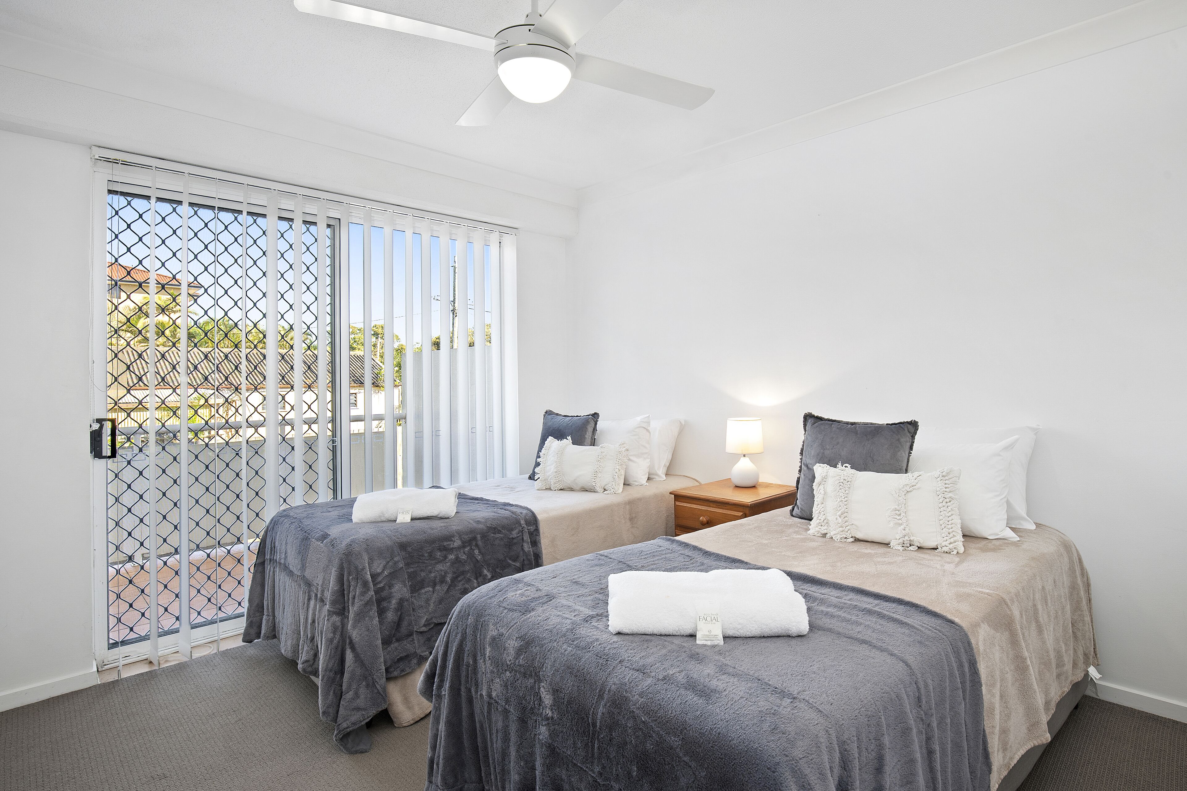 Habitación de hotel con dos camas, ventilador de techo, ventana con persianas y vista al exterior.