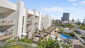 Et moderne hotel med flere balkoner, en swimmingpool og frodig beplantning.