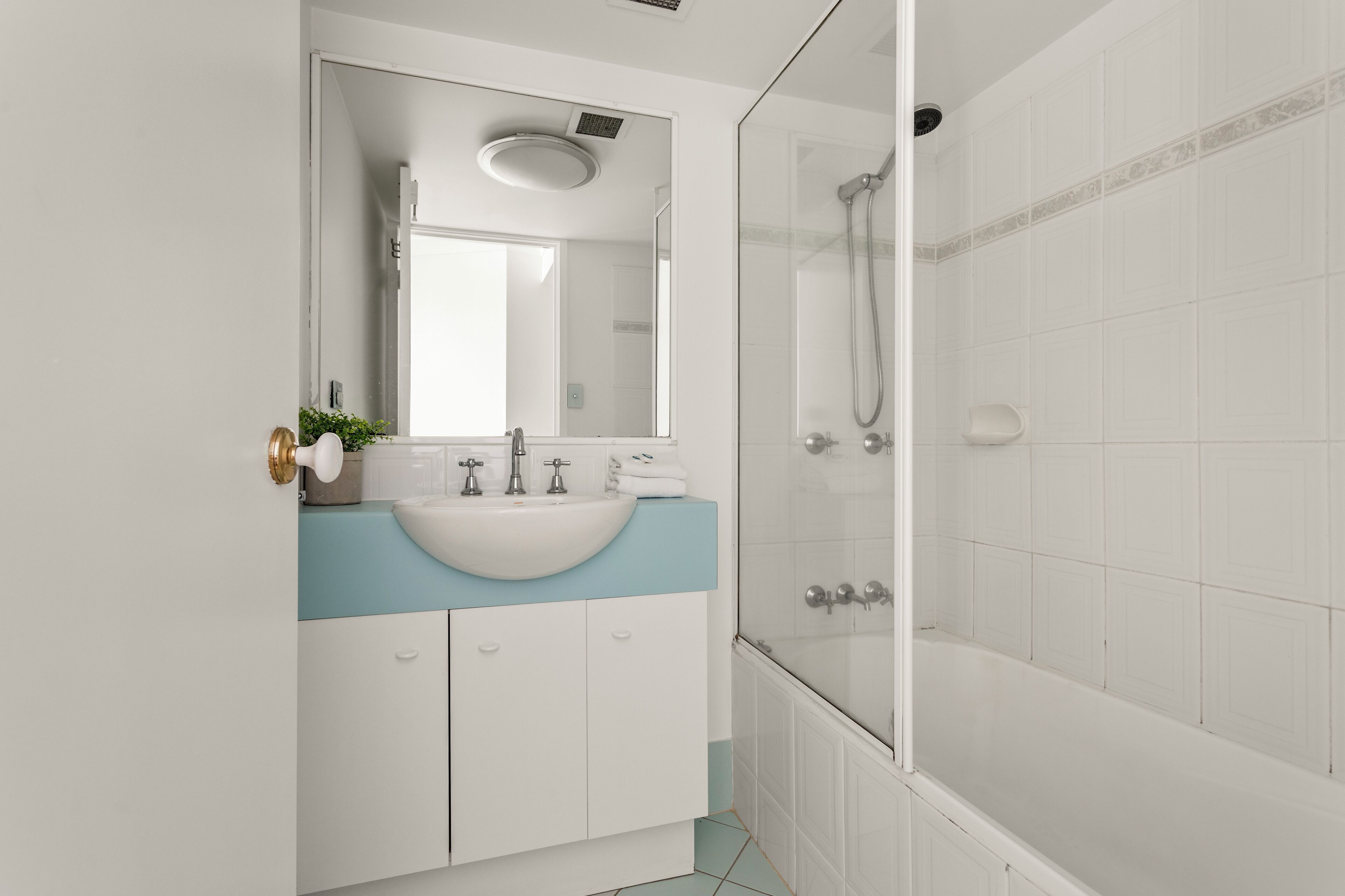A modern bathroom with a white sink, blue countertop, and a glass-enclosed shower.