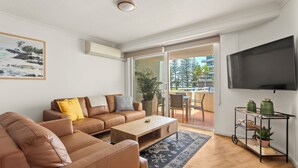 En moderne stue med en brun lædersofa, et træsofabord og et fjernsyn ophængt på væggen.