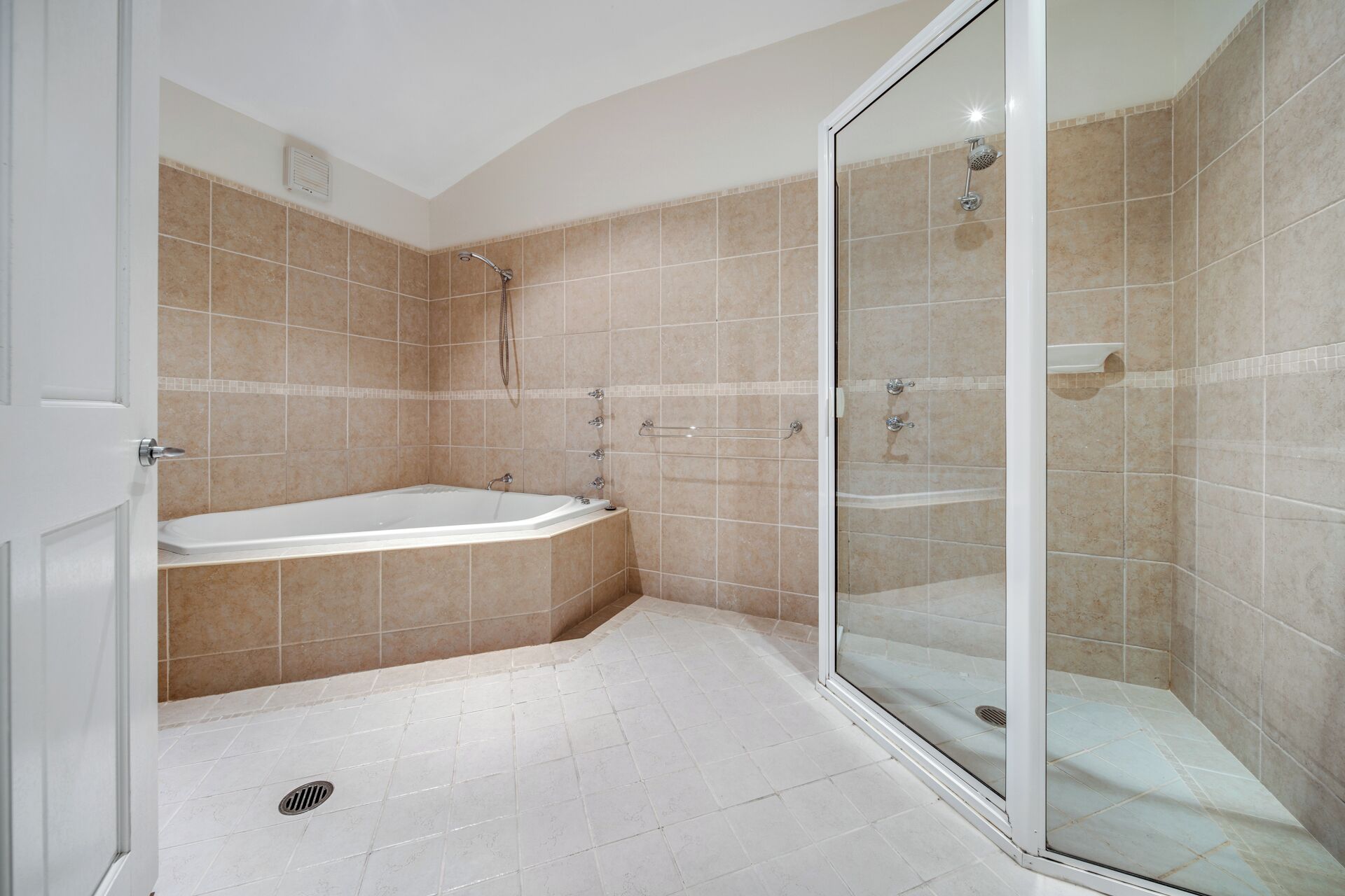 A bathroom with a bathtub, a glass-enclosed shower, and beige tiled walls.
