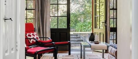 A room with a red chair, a sofa, a small table, and a view of greenery outside.