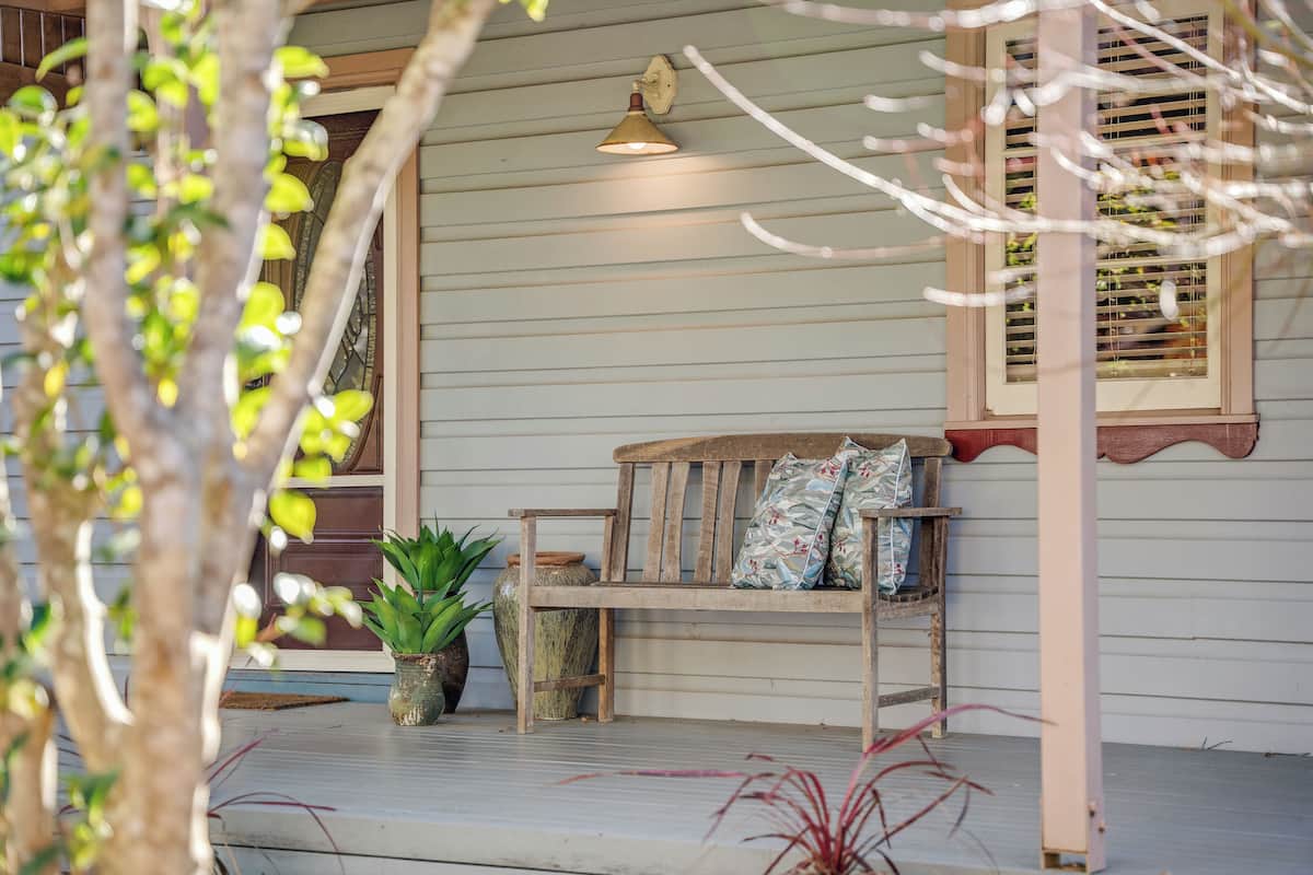 A porch with a wooden bench, a potted plant, and a wall-mounted light fixture.