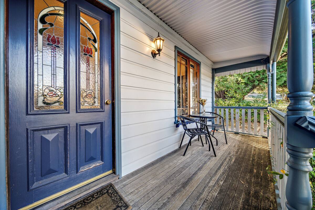 A wooden porch with a dark blue door, white siding, and a small table with chairs.
