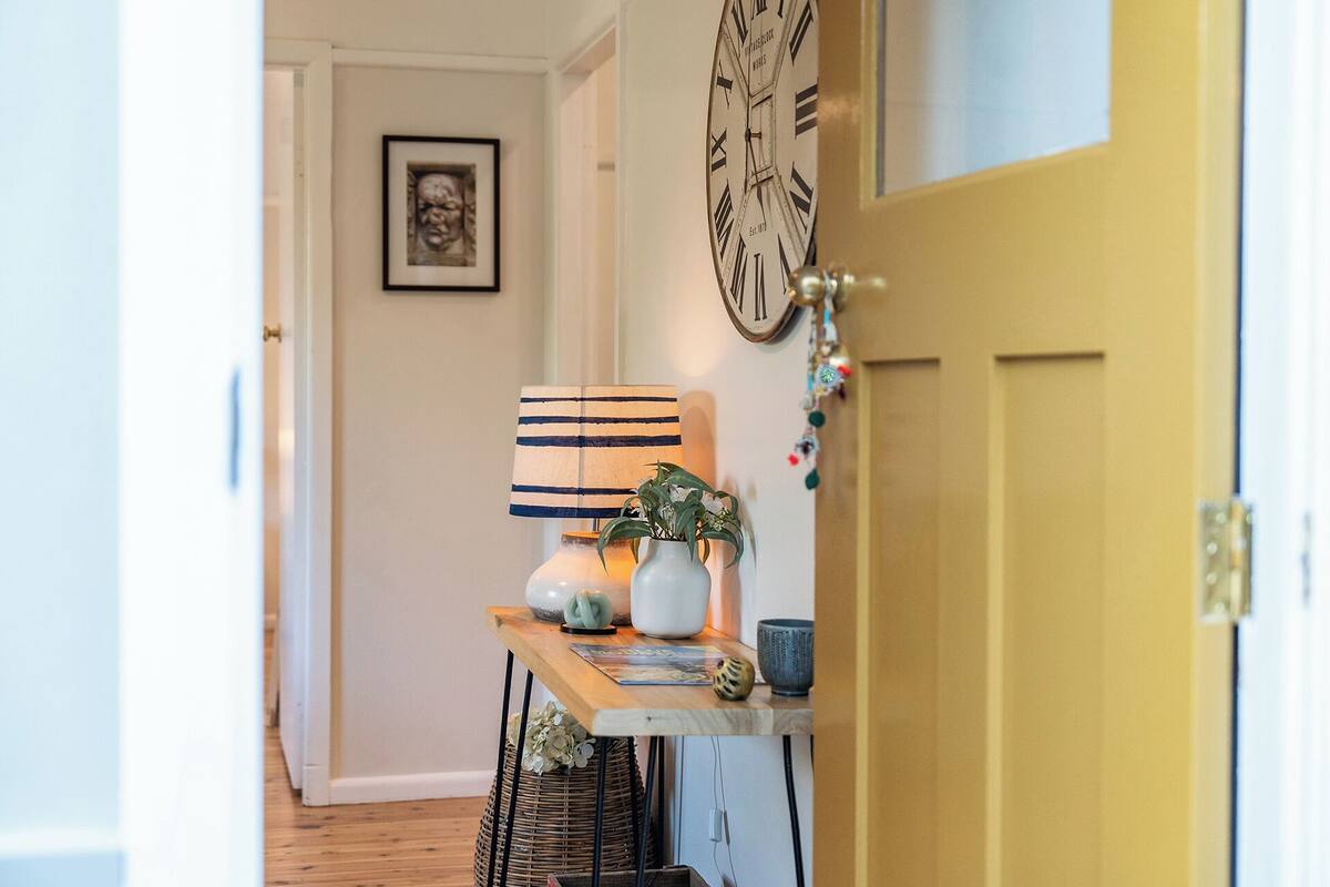 A hallway with a wooden table, a clock, and a framed picture on the wall.