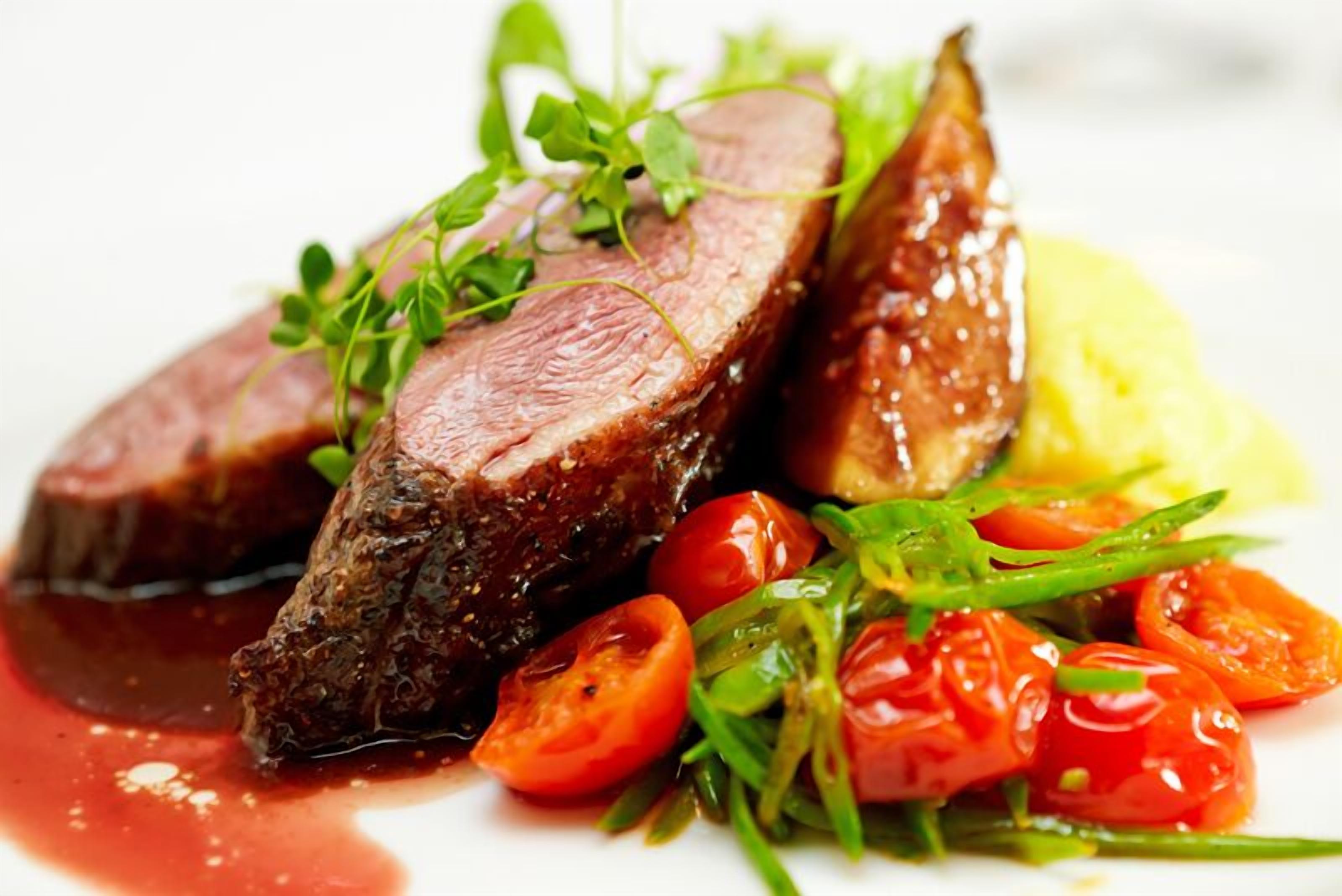 A plate of food with slices of meat, cherry tomatoes, and greens.