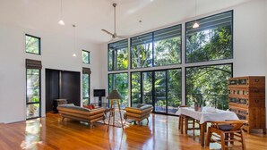 A spacious room with large windows, a ceiling fan, and a dining area with wooden furniture. - Pethers Rainforest Retreat (Tamborine Mountain)