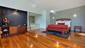 A modern bedroom with a wooden floor, a large bed with red bedding, a wooden nightstand, and a small table. - Pethers Rainforest Retreat (Tamborine Mountain)