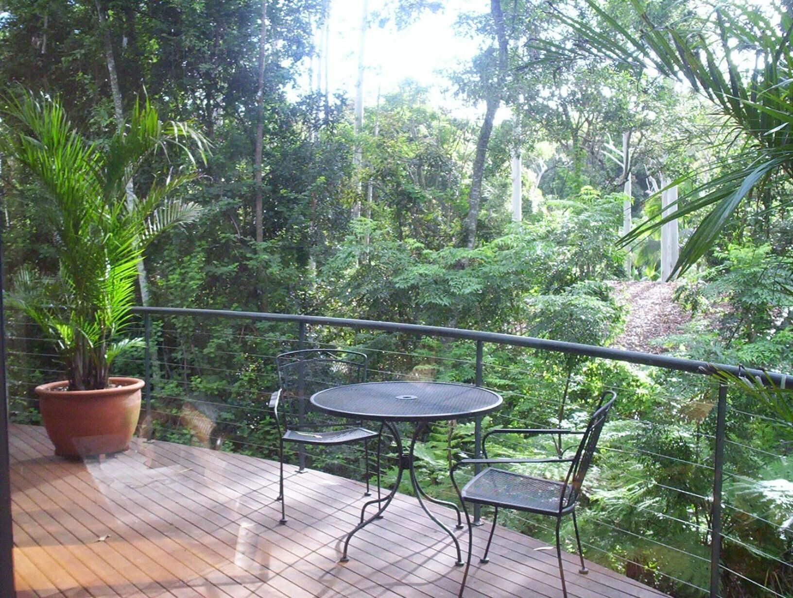 A balcony with a table and chairs, surrounded by lush greenery.
