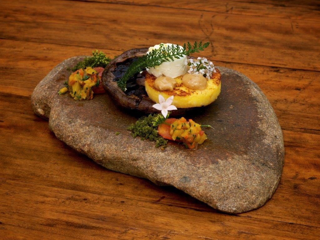 A stone table with a heart-shaped arrangement of food, including a grilled mushroom, a dollop of cream, and a small flower.