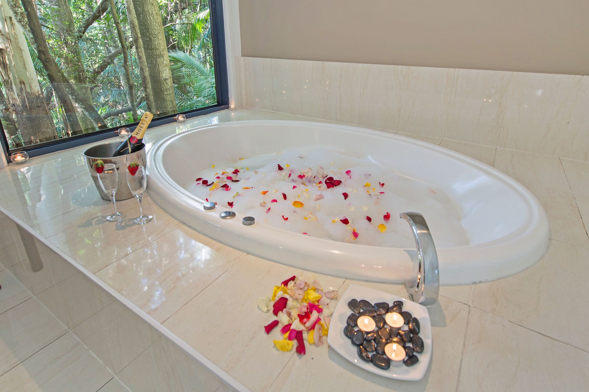A bathtub with rose petals and candles, a glass of champagne, and a bucket with a bottle.