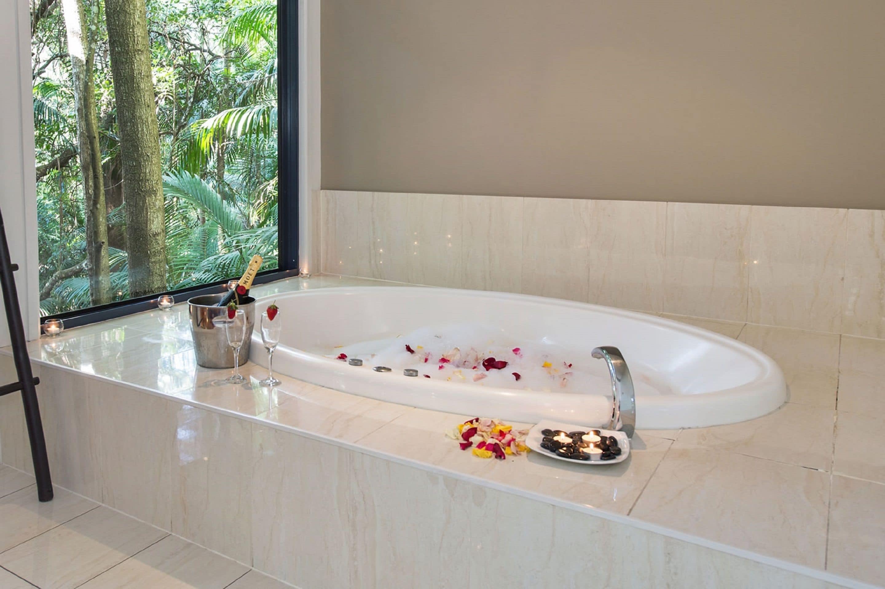 Un baño moderno con una bañera grande, una ventana con vistas a zonas verdes y suelo de mármol.