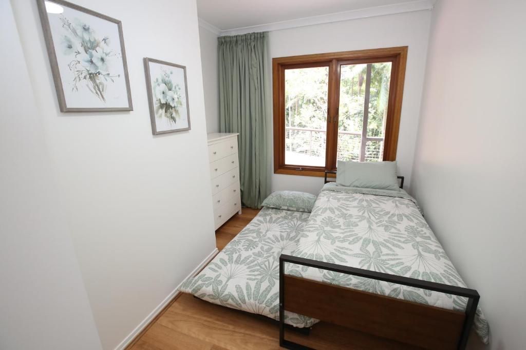 A bedroom with a bed, a dresser, a window with curtains, and two framed floral artworks on the wall.