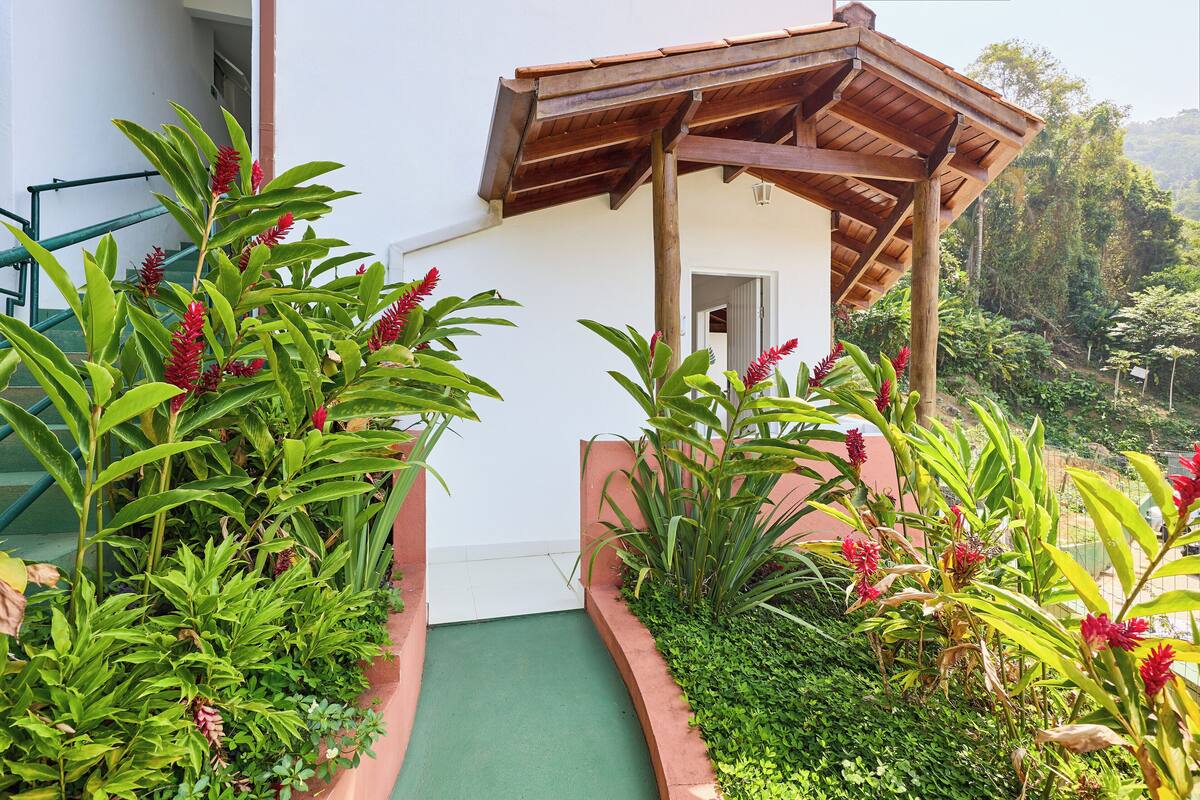 A pathway leading to a building with a wooden pergola and lush greenery.